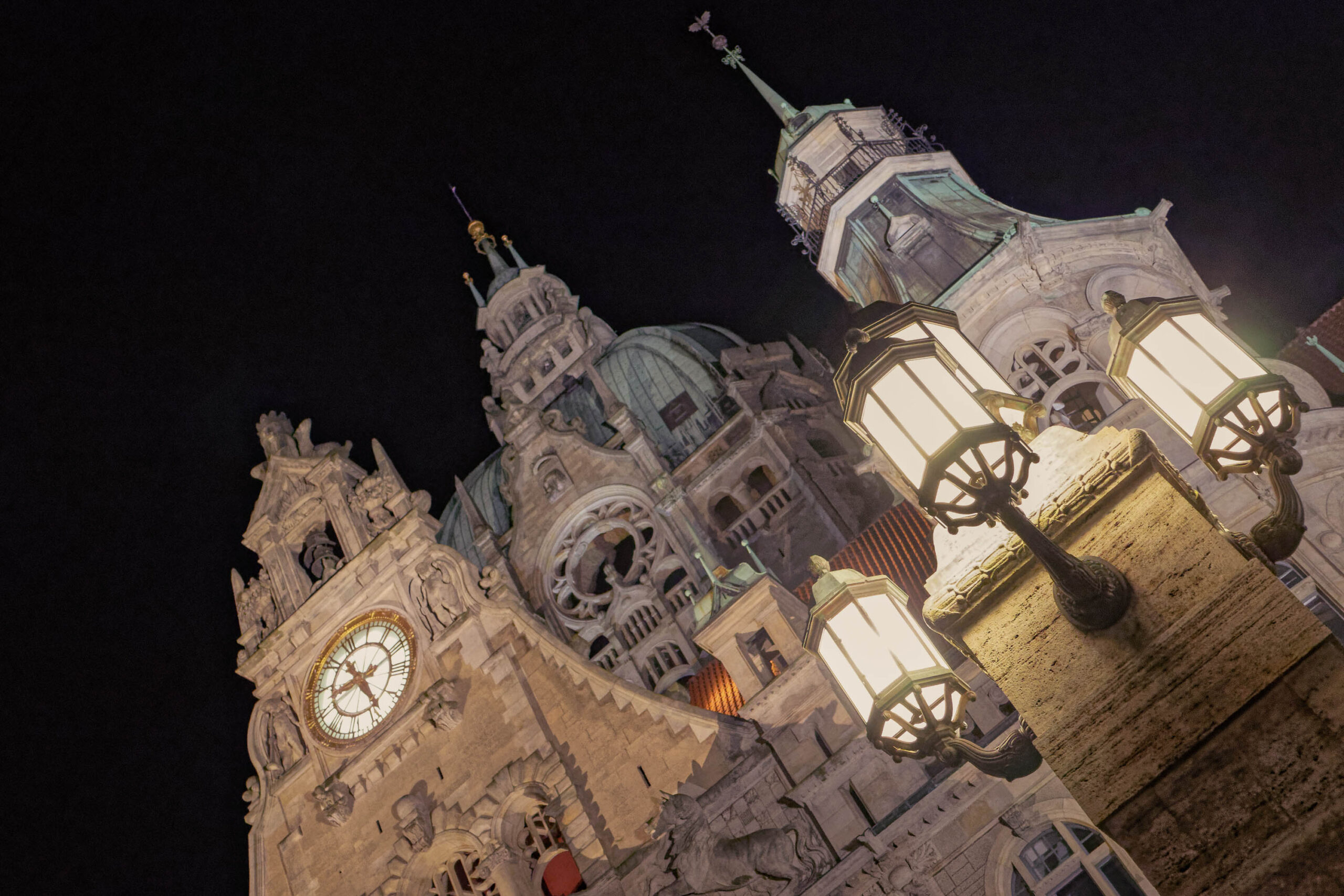 Das Foto zeigt eine ungewöhnliche, schräge Perspektive der Marktkirche in Hannover bei Nacht. Die Kirche ist beleuchtet, wobei die Fassade in einem warmen, goldenen Farbton erstrahlt. Die Beleuchtung betont die filigranen Details der Architektur. Die schräge Perspektive erzeugt ein dynamisches und fast surreal wirkendes Bild. Der Himmel ist tiefschwarz, was die Kirche noch stärker hervorhebt. Die Kirche wirkt monumental und imposant.
