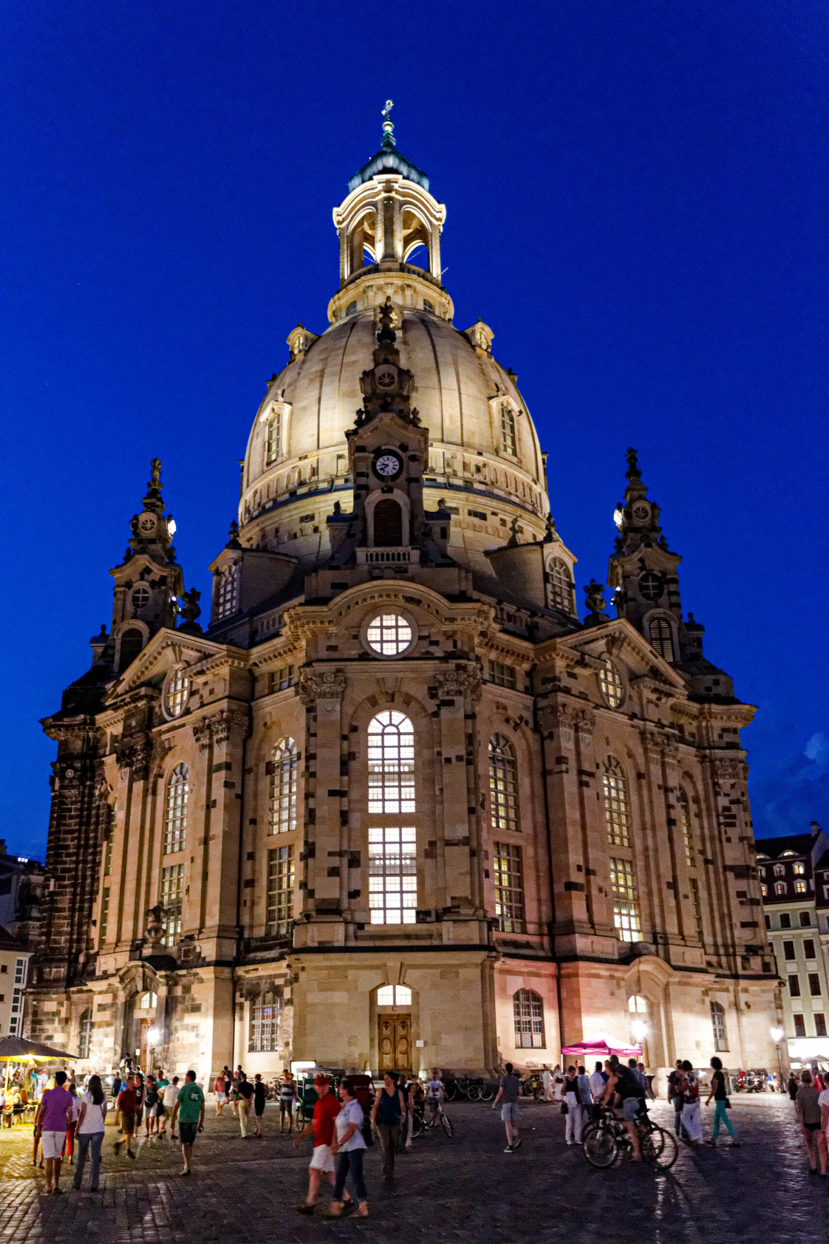 Das Foto zeigt die Frauenkirche in Dresden bei Nacht. Die Kirche ist vollständig beleuchtet und strahlt in einem warmen Goldton. Um die Kirche versammeln sich zahlreiche Menschen, die die Atmosphäre genießen. Der Himmel ist tiefblau und klar, was die Beleuchtung der Kirche noch verstärkt. Das Foto wurde wahrscheinlich im August 2013 aufgenommen, kurz nach der Restaurierung der Kirche.