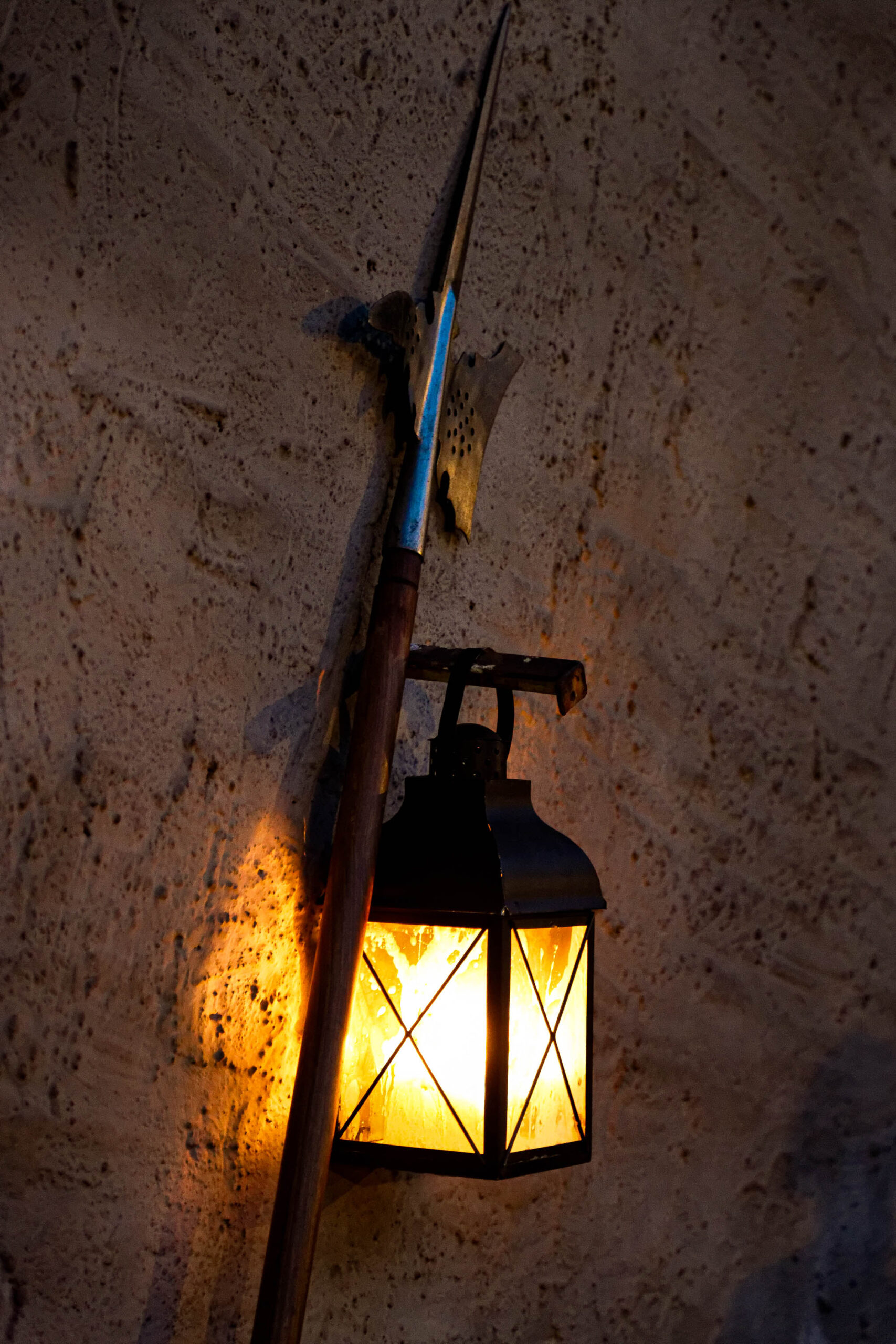 Das Bild zeigt eine Laterne, die an einer Wand in Dresden befestigt ist. Die Laterne ist aus Metall gefertigt und hat ein quadratisches Glasfenster, das ein warmes, gelbes Licht abgibt. Die Wand ist aus grobem Stein und hat eine raue Textur. Die Beleuchtung ist warm und gemütlich, was eine ruhige und friedliche Atmosphäre schafft. Das Bild wurde im August 2013 aufgenommen.